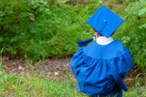 A little boy dressed in a blue graduation cap and gown.